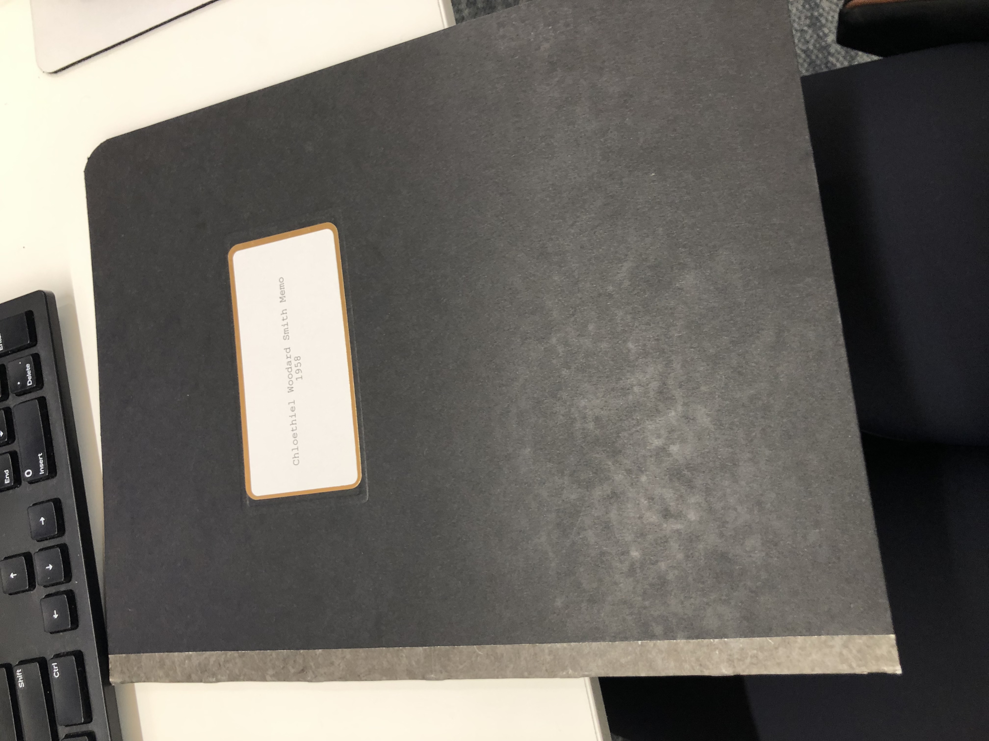 Photograph of a black folder with a white label that reads “Chloethiel Woodard Smith Memo, 1958.”