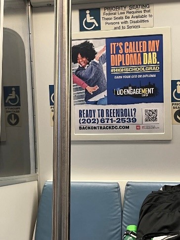Photograph of a QR code that rests on the bottom right corner of a semi-large enrollment poster advertisement mounted on the wall inside of a DC metro car. The words next to the code read “Ready to Reenroll?”