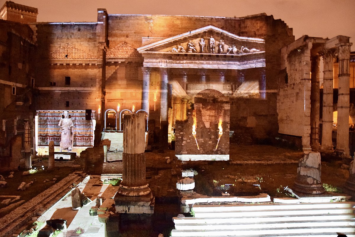 Photograph of the ruins of the Roman Forum at dusk. The facade of a temple and brightly painted walls are projected on the face of the walls and the broken tile floor.