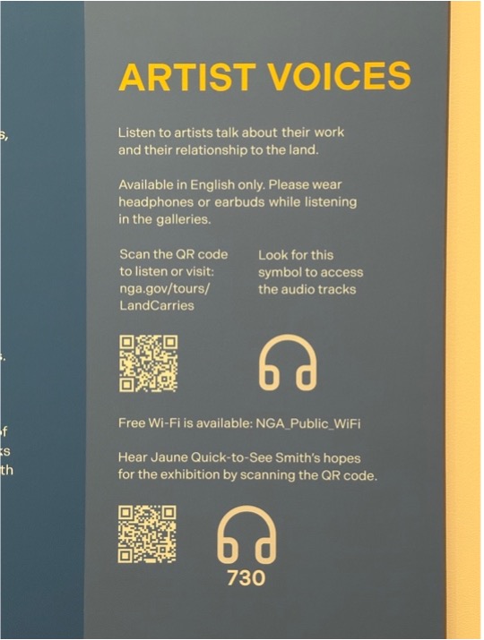 Wall text titled “Artist Voices,” two white QR codes on blue background with headphone icons to the right. “Hear Jaune Quick-to-See Smith's hopes for the exhibition by scanning the QR code” is printed above the bottom QR code, and the number 730 is printed below.